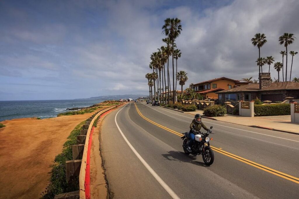 White 2023 Royal Enfield Hunter being ridden through an empty road next to the beach in California