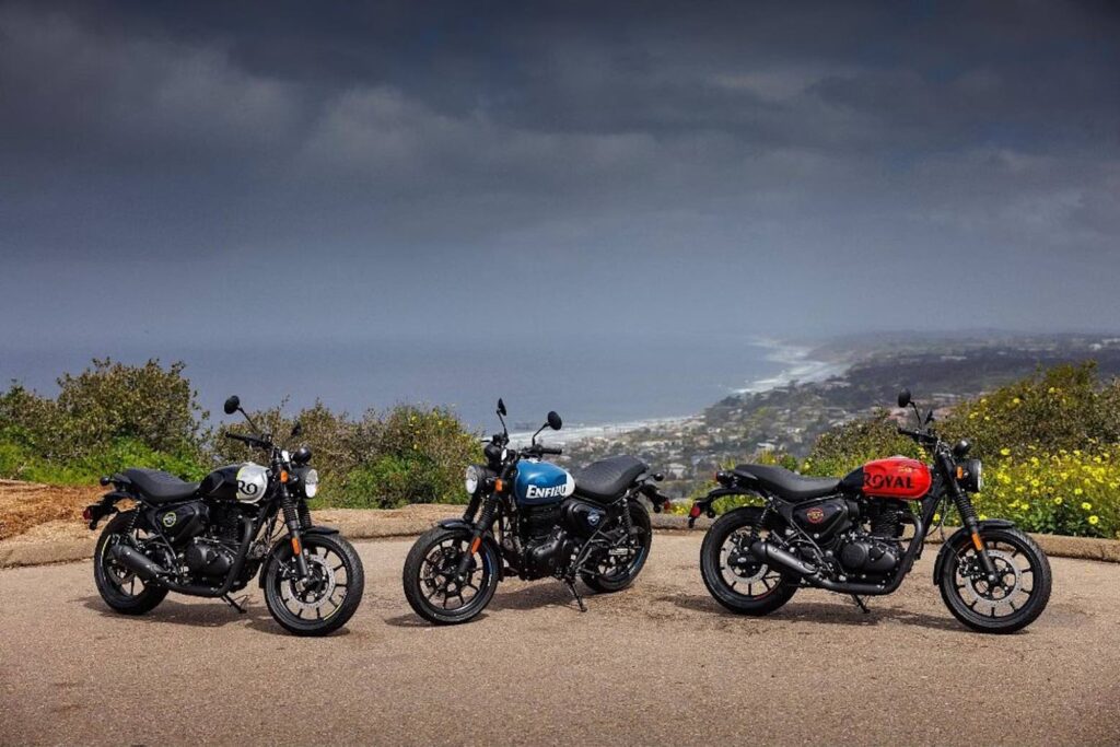 Three 2023 Royal Enfield Hunter parked on the side of the road overlooking a beach, showing the black, blue and red colours available
